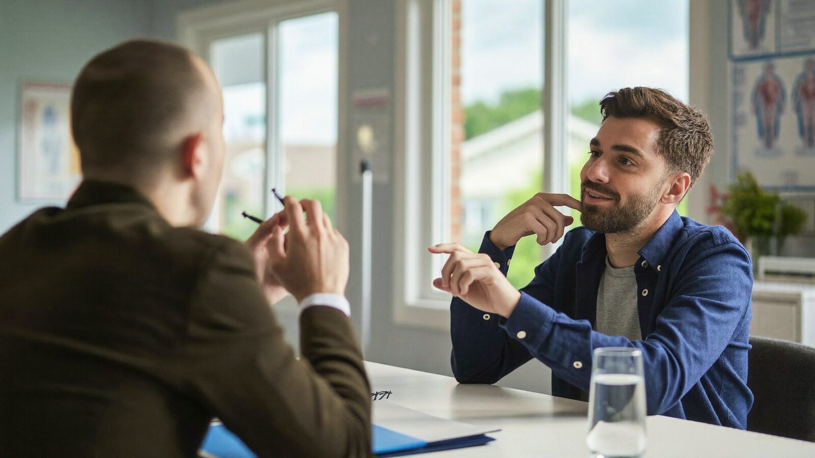 Man in his 30s talking with a doctor in a bright consultation room, both seated, in a friendly conversation