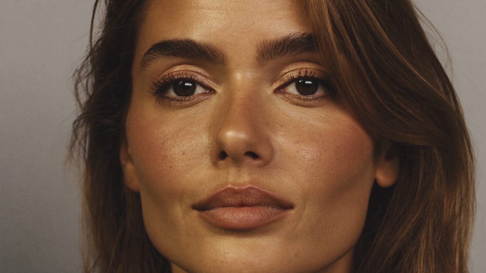 Close portrait of a woman in her 30s with full, natural, well-shaped eyebrows in soft studio light