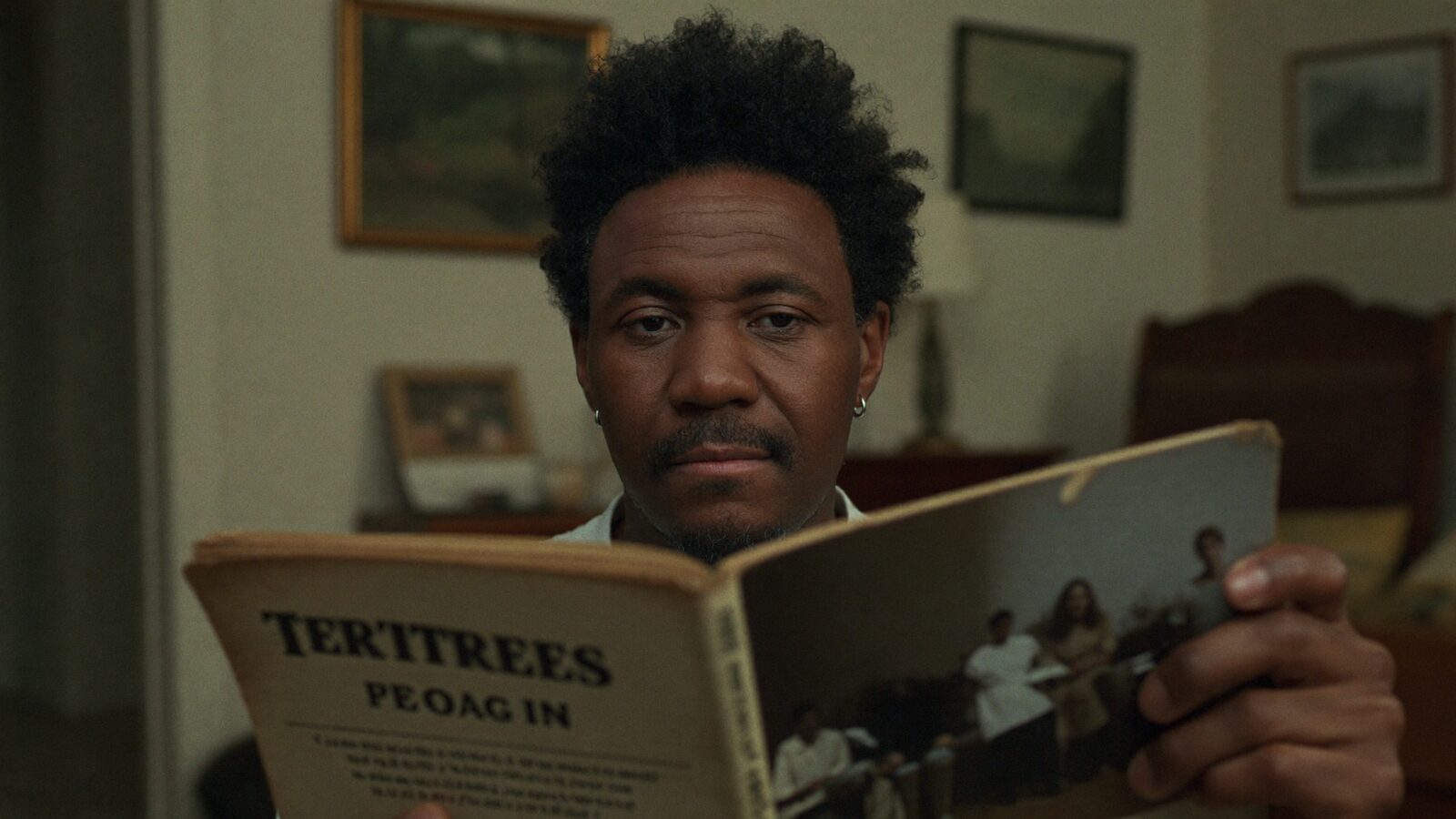 A man in his 50s with a natural full hairline holding an old family photo album in warm living room light