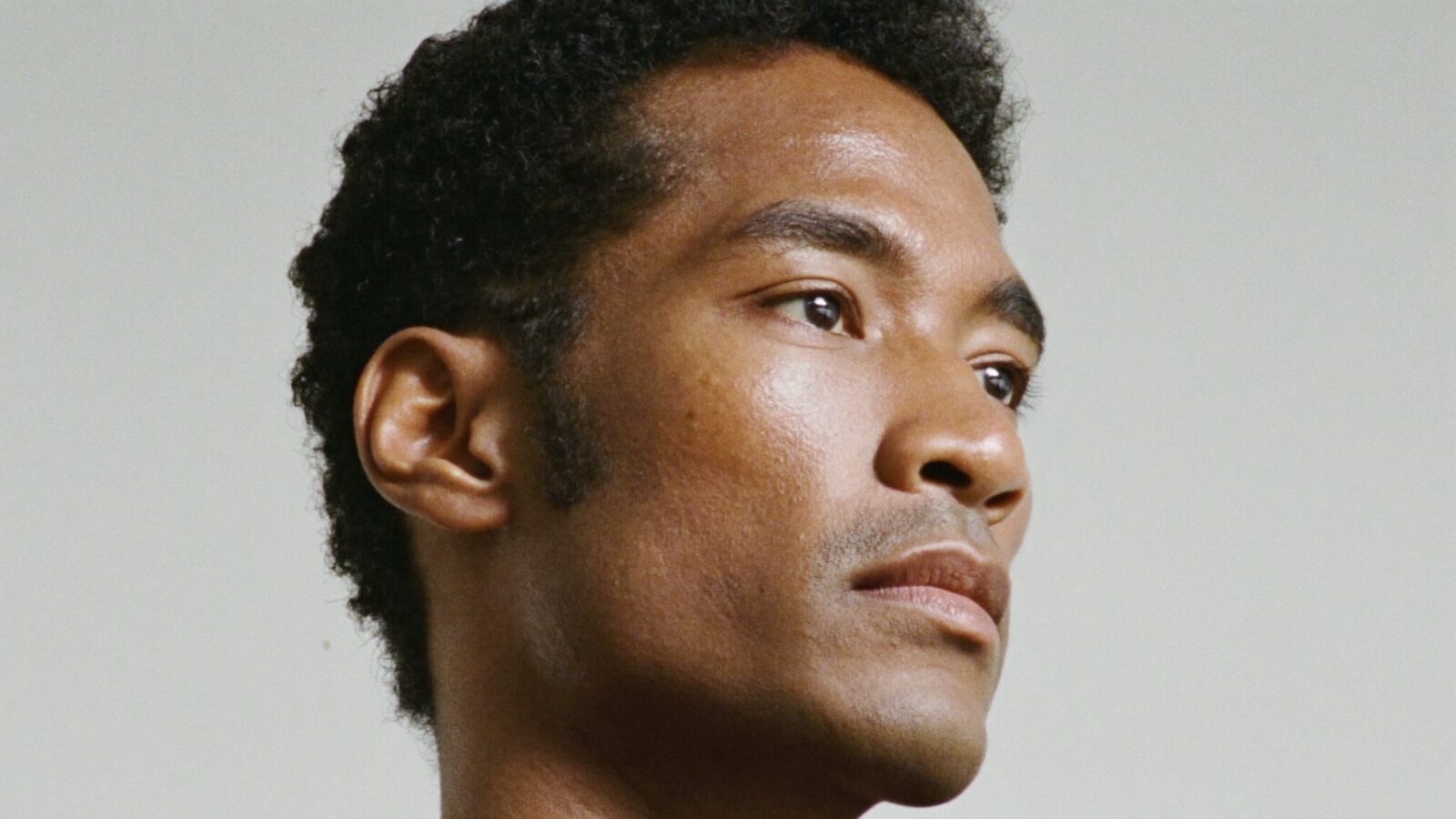 Portrait of a man in his 30s with a natural, well-defined hairline, three-quarter view, plain light background
