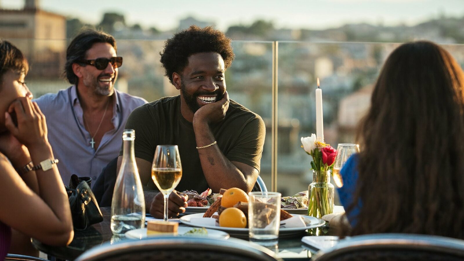Confident man in his 40s with a full natural hairline laughing with friends on a rooftop terrace at golden hour