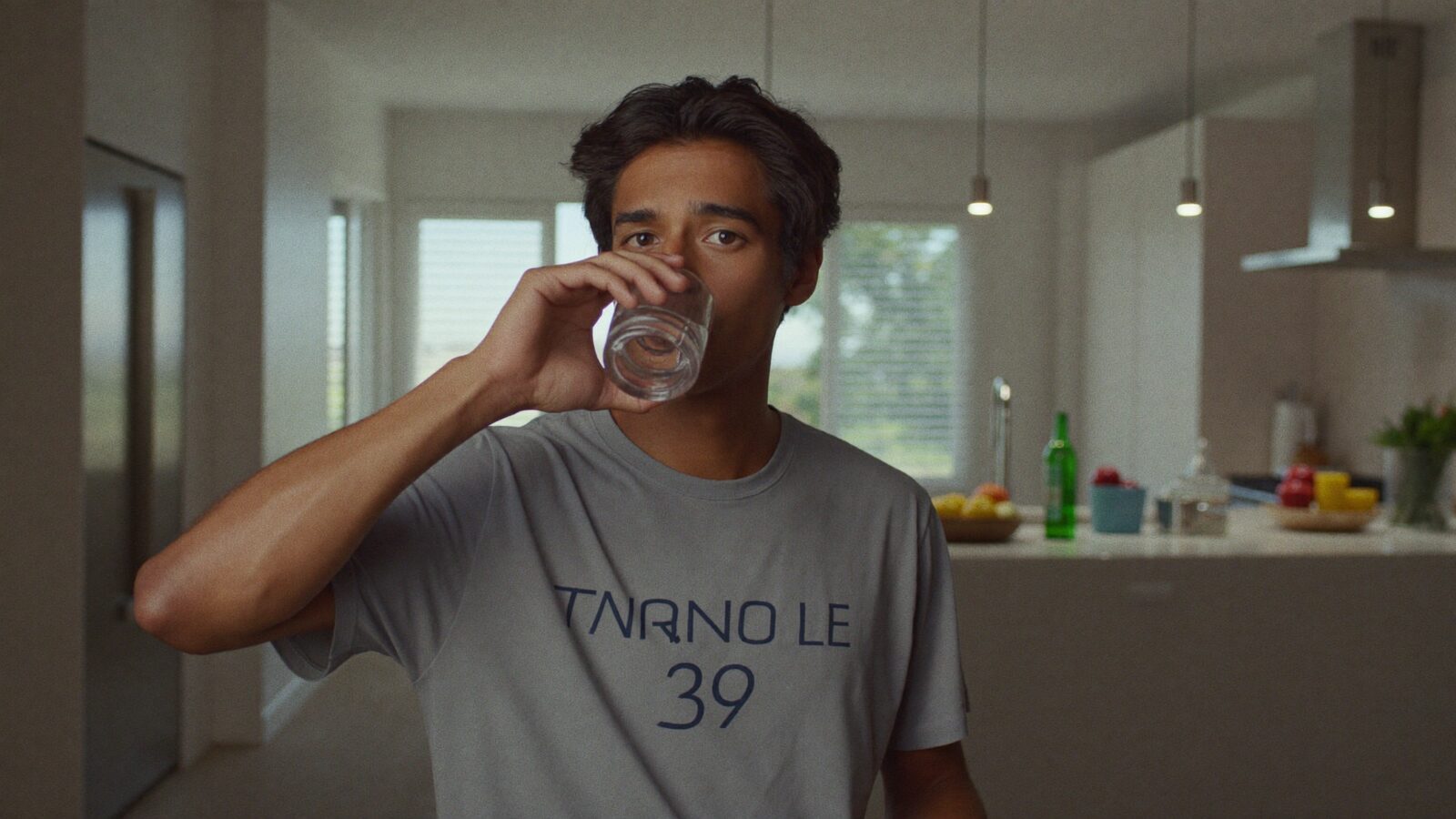 Man in his 30s with full hair holding a glass of water in a bright modern kitchen during his morning routine