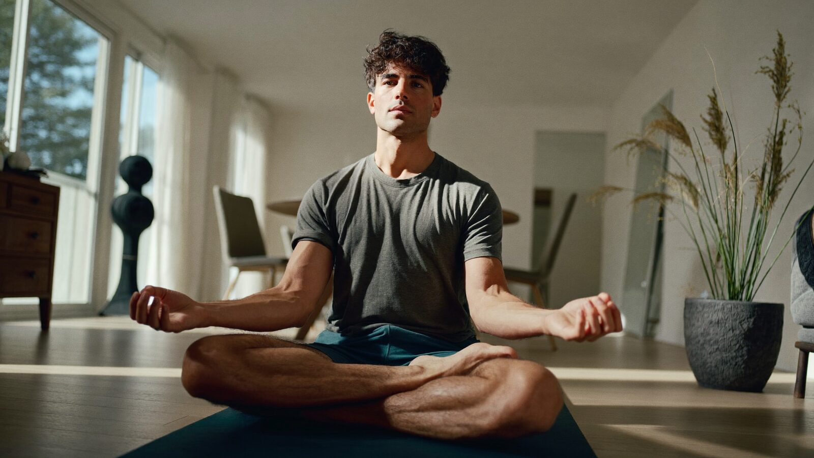 Man in his 30s with healthy thick hair stretching on a yoga mat in a bright apartment