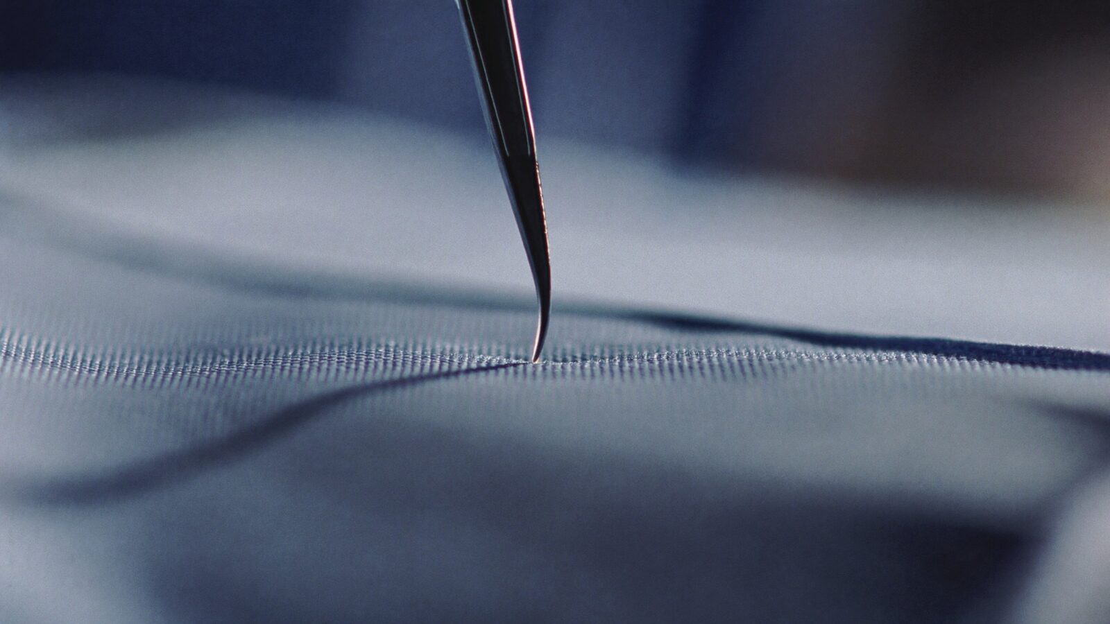 Macro close-up of a tiny clear blade tip on a sterile blue surgical cloth in clean clinical light