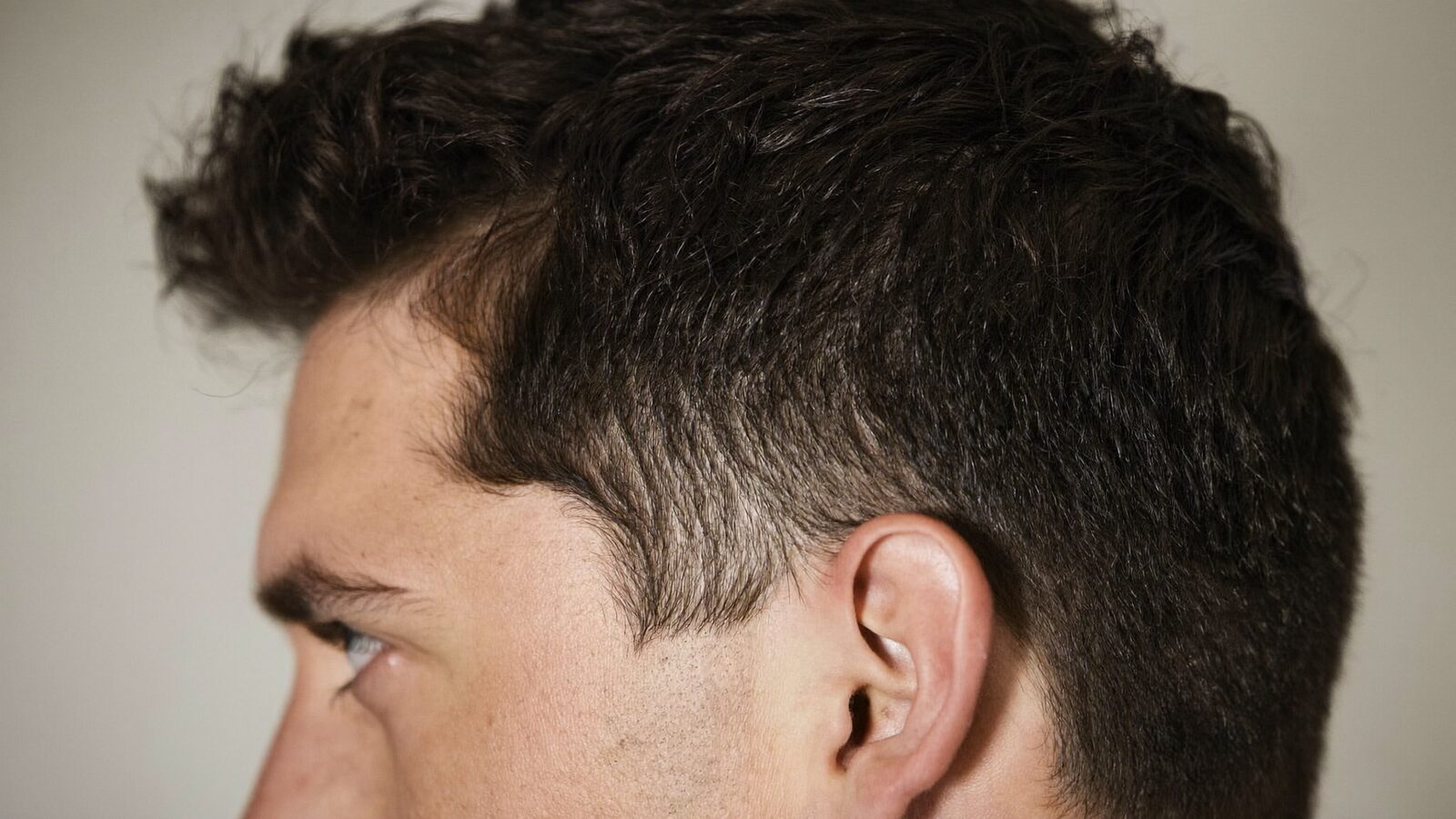 Close side profile of a man in his 30s showing a sharp, natural temple and sideburn line in soft studio light